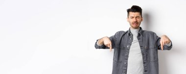 Üzgün, ağlayan, parmaklarını yere doğru gösteren, hayal kırıklığına uğramış, kötü haberler veren, beyaz arka planda üzgün duran adam..