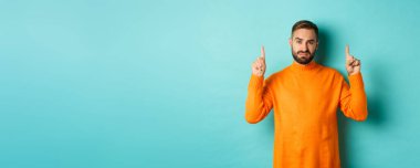 Şüpheci ve gönülsüz bir adam hoşnutsuz görünüyor, parmakla işaret ediyor, kötü bir teklif, turkuaz arka planda duruyor..