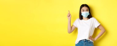 Covid, sağlık ve salgın hastalık konsepti. Tıbbi maskeli Asyalı kadın manken ve beyaz tişört sol üst köşedeki logoyu işaret ediyor..