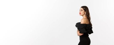 Kırmızı dudaklı, makyajlı ve siyah elbiseli zarif genç bir kadının profil görüntüsü. Uzaktan bakınca rüya gibi görünüyor. Beyaz arka planda duruyor..