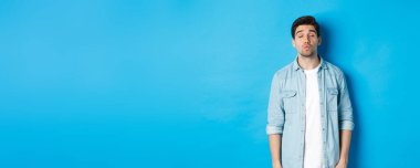 Yakışıklı bir adam öpüşmeyi bekliyor, dudaklarını büzüyor, gözlerini kapatıyor ve mavi arka planda duruyor..