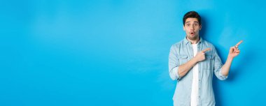 Gayri resmi kıyafetli, şaşırmış sakallı adamın portresi. Parmakla göstererek harika bir tanıtım teklifi sunuyor. Mavi arka planda duruyor..