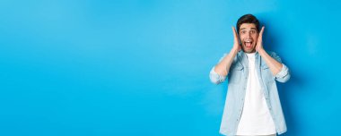 Korkmuş bir adam çığlık atıyor ve bir şeye bakıyor, mavi arka planda duruyor..