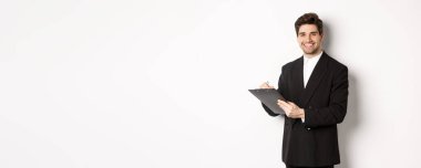 Siyah takım elbiseli kendine güvenen bir işadamının portresi, evrakları imzalıyor ve gülümsüyor, beyaz arka planda mutlu duruyor..