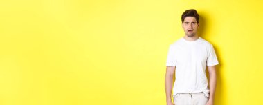 Kafası karışmış ve kafası karışmış bir adamın görüntüsü bir şeyi anlayamaz, kaşlarını çatar ve şaşkın bakar, sarı arka planda durur..