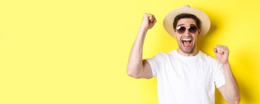Turizm ve tatil kavramı. Tatilini kutlayan mutlu erkek turist, elini kaldırıyor ve sevinç çığlıkları atıyor, hasır şapkalı güneş gözlüğü takıyor..