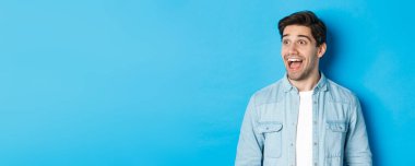 Yakışıklı beyaz erkek modelin yakın plan çekimi solu şaşırtır, reklamları kontrol eder, mavi arka planda durur..