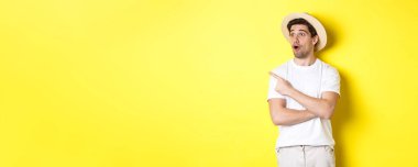 Turizm ve yaşam tarzı kavramı. Hasır şapkalı heyecanlı yakışıklı adam reklama bakıyor, sol üst köşedeki logoya bakıyor, sarı arka plan..