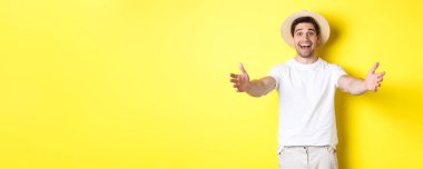 Turizm ve yaz kavramı. Mutlu ve dost canlısı gezgin elini uzatıp sarılır, selamlar ya da hoş geldin der, sarı arka planda durur..