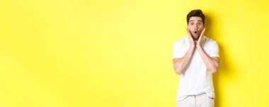 Yakışıklı adamın görüntüsü şaşırmış, soluk soluğa kalmış ve diyor ki vay canına, tanıtıma bakıyor şaşırmış, sarı arka planda duruyor..