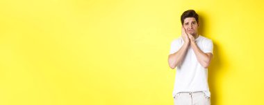 Üzgün adam diş ağrısından şikayetçi, kırlangıç yanağına dokunuyor ve üzgün görünüyor, sarı arka planda duruyor. Boşluğu kopyala