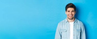 Genç bir adamın kendini garip hissettiği yakın plan. Rahatsız edici bir durumdan gülümse ve kork. Mavi arka planda dur..