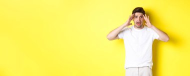 Şok olmuş, paniklemiş, el ele tutuşmuş, sarı arka planda duran sinirli bir adam..