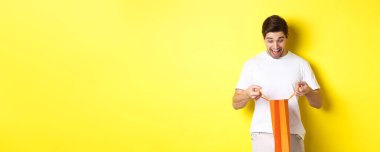 Heyecanlı adam hediyeli çantayı açtı, şaşırmış ve mutlu bir yüzle içeriye baktı, sarı arka planda duruyordu..