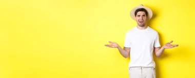 Turizm ve yaz kavramı. Kafası karışmış gezgin omuz silkiyor, bir şey anlayamıyor, sarı arka planda duruyor..