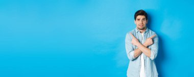 Tedirgin bir adamın portresi parmaklarını yana doğru gösteriyor, kararsız görünüyor ve seçimle ilgili yardım istiyor, sol ve sağ promosyon tekliflerini gösteriyor, mavi arka planda duruyor..