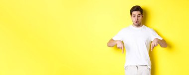 Endişeli adam işaret ediyor ve aşağı bakıyor, sarı arka planda ürkmüş duruyor..