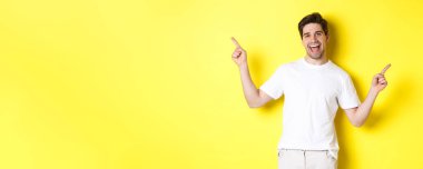 Mutlu stil sahibi adam iki farklı şey gösteriyor. Sol ve sağ tanıtımlarda parmaklarını yana doğru gösteriyor. Sarı arka planda duruyor..