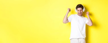 Beyaz kulaklıklarla dans eden ve müzik dinleyen mutlu bir adam, sarı arka planda duruyor. Boşluğu kopyala