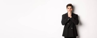 Şok olmuş takım elbiseli yakışıklı iş adamının portresi, korkunç bir duruma tepki veriyor, nefes nefese kalıyor ve elleriyle ağzını kapatıyor, beyaz arka planda ürküyor..