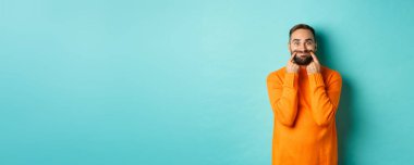 Sakallı bir adamın mutlu bir gülümsemeyle dudaklarını germesi, sahte mutluluk, açık mavi arka planda durması..