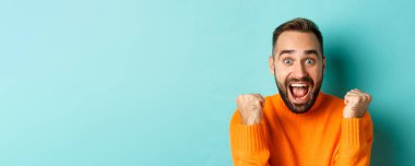 Tatmin olmuş yakışıklı bir adamın görüntüsü, kazanmanın sevinci ya da başarının sevinci, yumruk tokuşturmak ve evet demek, turkuaz arka planda durmak..