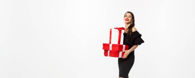 Siyah elbiseli, kırmızı dudaklı, elinde Noel hediyeleri ve gülümseyen mutlu, beyaz arka planda duran zarif bir kadın..