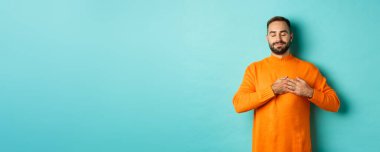 Yakışıklı adam nostaljik hissediyor, kalbi tutuyor ve hayal kuruyor, bir şeyleri hatırlıyor ya da hayal ediyor, turkuaz arka plana karşı kaygısız duruyor..