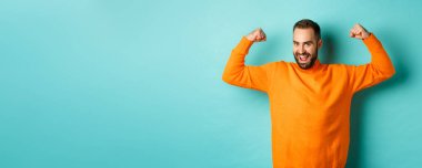 Genç ve güçlü görünümlü, kendinden emin, kaslı, kaslı, kendine güvenen, açık mavi arka planda duran genç ve güçlü bir adam..