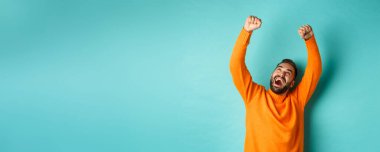 Zafer kazanan, zaferi kutlayan, açık mavi arka planda duran mutlu bir adam. Boşluğu kopyala