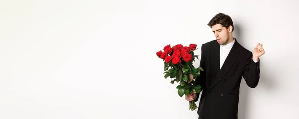 stock image Image of elegant and sassy man in black suit, looking confident and holding bouquet of red roses, going on a romantic date, standing against white background.