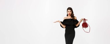 Güzellik ve moda konsepti. Hayal kırıklığına uğramış, kafası karışmış, kafası karışmış, kafası karışmış, şaşkın, parti elbisesi ve yüksek topuklu ayakkabılar giyen bir kadın..