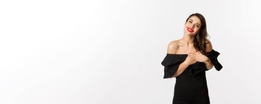 Moda ve güzellik. Siyah elbiseli çekici kadın teşekkür ediyor, gülümsüyor ve mutlu duygularla el ele tutuşuyor, beyaz arka plan..