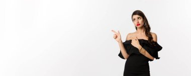 Moda ve güzellik. Siyah elbiseli, kıskanç, çekici bir kadın solu işaret ediyor, hayal kırıklığına uğramış, beyaz arka planda..
