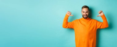 Yakışıklı, kendine güvenen, kendine güvenen turuncu süveter giyen, açık mavi arka planda duran kendine güvenen bir adam..