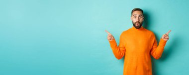 Alışveriş ve reklam konsepti. Heyecanlı adam alıcı parmaklarını yana doğru gösteriyor, iki seçenek sunuyor, sol ve sağ pankartlar, açık mavi arkaplanın üzerinde duruyor.