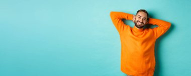 Yakışıklı adam rahatlıyor, dinleniyor ve gülümsüyor, tasasız yüzüyle el ele tutuşuyor, açık mavi arka planda duruyor..