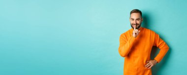 Mutlu adam sesini alçalt, sus ve gülümse, sürprize hazırlan, kameraya sus, turkuaz arka planda dur..