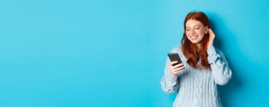 Teknoloji. Mutlu kızıl kız cep telefonundan memnun görünüyor. Mesajda iltifat okuyor. Gülümsüyor ve saçlarını kulaklarının arkasına sokuyor..