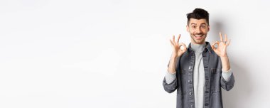 Mutlu adam evet diyor, gülümsüyor ve iyi işaretler gösteriyor, iyi ürün gibi, onaylamak için başını salla ve tatmin ol, mükemmel bir iş çıkarıyorsun, beyaz arka planda duruyorsun..