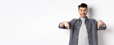 Bıyıklı, mutlu, beyaz bir adam. Gülümsüyor ve özel bir anlaşma yapıyor. Buraya bakmaya davet ediyor, beyaz arka planda duruyor..