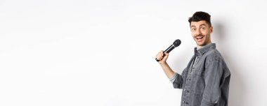 Mikrofon tutan yakışıklı bir adamın profili. Heyecanlı yüzüyle kameraya dön, karaoke yap ve stand-up yap, beyaz arka planda dur..
