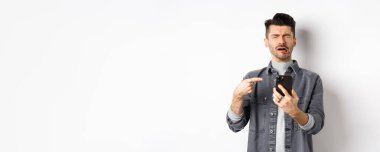 Üzgün, ağlayan, akıllı telefonu işaret eden, hıçkıra hıçkıra ağlayan, şikayet eden ya da mutsuz hisseden, beyaz arka planda duran adam..