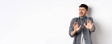 - Benden uzak dur! Korkmuş genç bir adam çığlık atıyor ve durmak istiyor, geri çekiliyor ve korkmuş görünüyor, kötü bir şeyi reddediyor, beyaz arka planda duruyor..