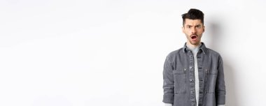 Şok olmuş ve gücenmiş bir adam, kameraya açık ağızla bakıyor, acımasız sözlerle incinmiş, beyaz arka planda hayal kırıklığına uğramış..