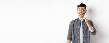 Mutlu komik adam büyüteçten büyük gözlerle bakıyor, ilginç bir anlaşmaya bakıyor, bir şeyler arıyor, beyaz arka planda duruyor..