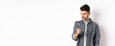 Ciddi araştırmacı, büyüteçle aşağı bakan, ciddi bakan, beyaz arka planda duran.