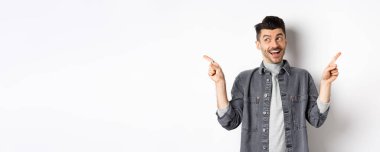 Mutlu stil sahibi adam gülüyor, yan yan işaret ediyor, iki seçenek gösteriyor, tanıtım teklifleri sunuyor ve gülümsüyor, beyaz arka plana karşı duruyor..