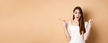Şaşırmış genç bir kız solu ve sağı işaret ediyor, nefes nefese ve hayret verici diyor, iki havalı seçenek gösteriyor, bej arka plan.