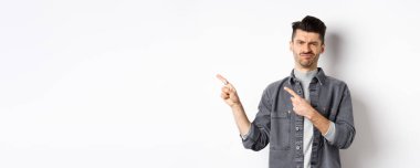 Şüpheci ve hayal kırıklığına uğramış genç adam solu işaret ediyor, reddedilerek kafasını sallıyor, kötü ürünlerden hoşlanmıyor, beyaz arka planda duruyor..